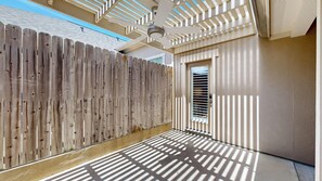 A covered outdoor area with a wooden fence, a door with a window, and a ceiling fan.