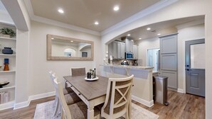 A dining area with a wooden table and chairs, a kitchen with cabinets and a microwave, and a door leading to another room.
