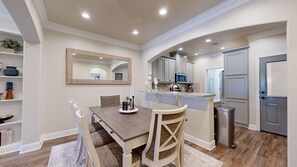A dining area with a wooden table and chairs, a kitchen with cabinets and a microwave, and a door leading to another room.