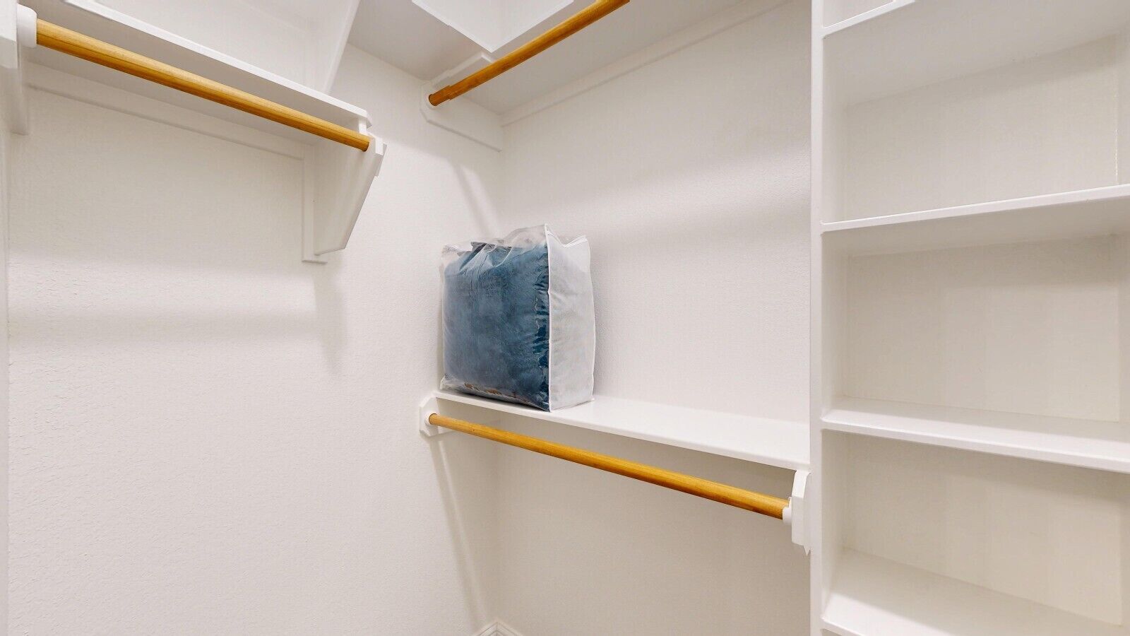 Ein Kleiderschrank mit weißen Wänden, Holzstangen und einer Plastiktüte auf einer der Regale.