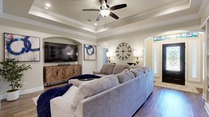 Una sala moderna con un sofá modular, televisor de pantalla plana, decoración en la pared, un reloj grande y una puerta con un vitral.