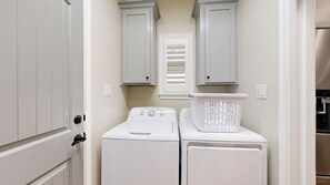 A laundry room with two white washing machines, a white laundry basket, and two white cabinets above the machines.