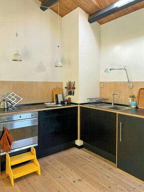 A kitchen with a stove, sink, hanging utensils, and a wooden stool. - Idyll on natural plot near beach in Odsherred (Vig)