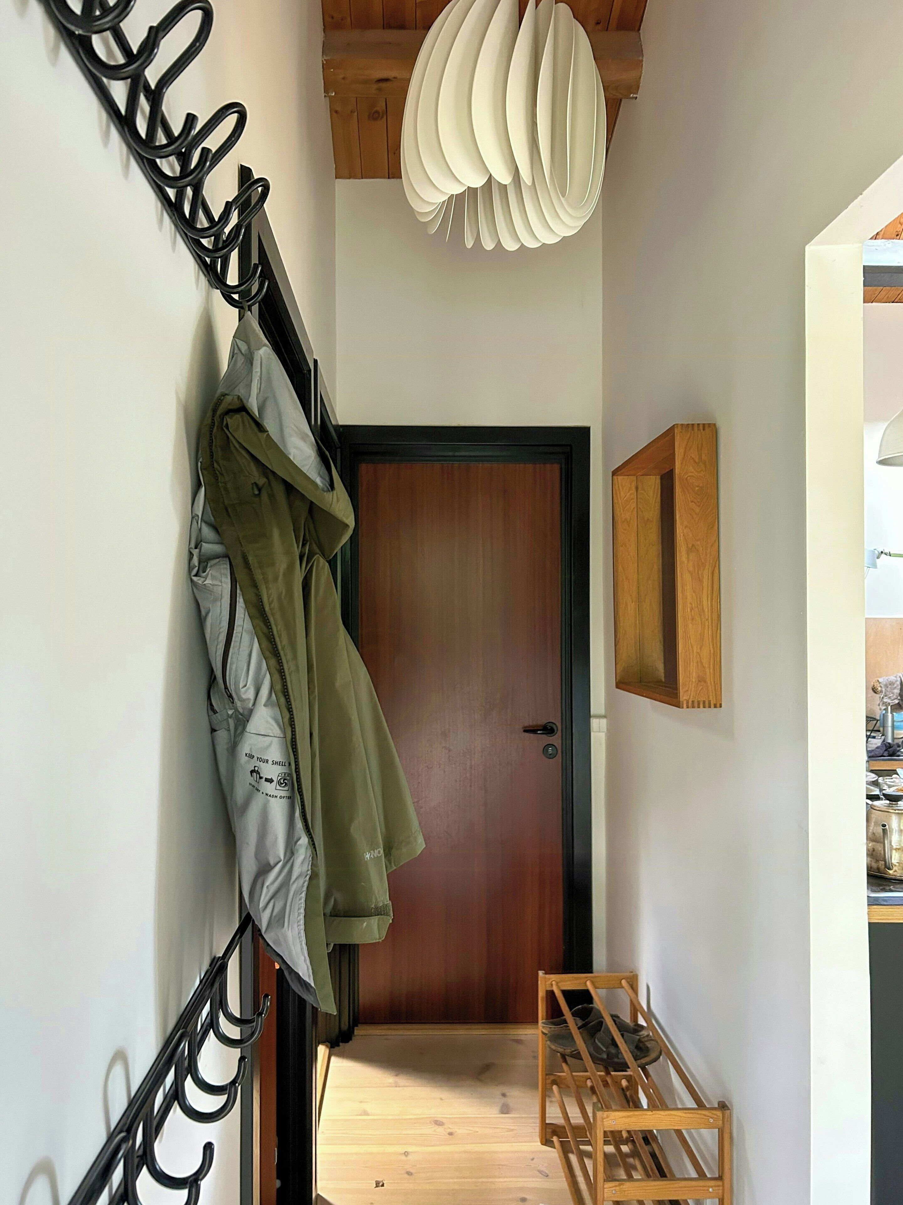 A hallway with a coat rack, a wooden door, and a small wooden table with shoes.