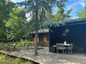 A wooden deck with a table and chairs, surrounded by trees. - Idyll on natural plot near beach in Odsherred (Vig)