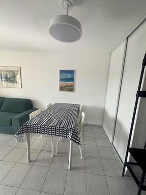 A room with a table set for dining, a green sofa, a framed picture on the wall, and a ceiling light fixture. - Stunning apartment with a view of the lagoon, 250 meters from the beach (Saint-Cyprien)