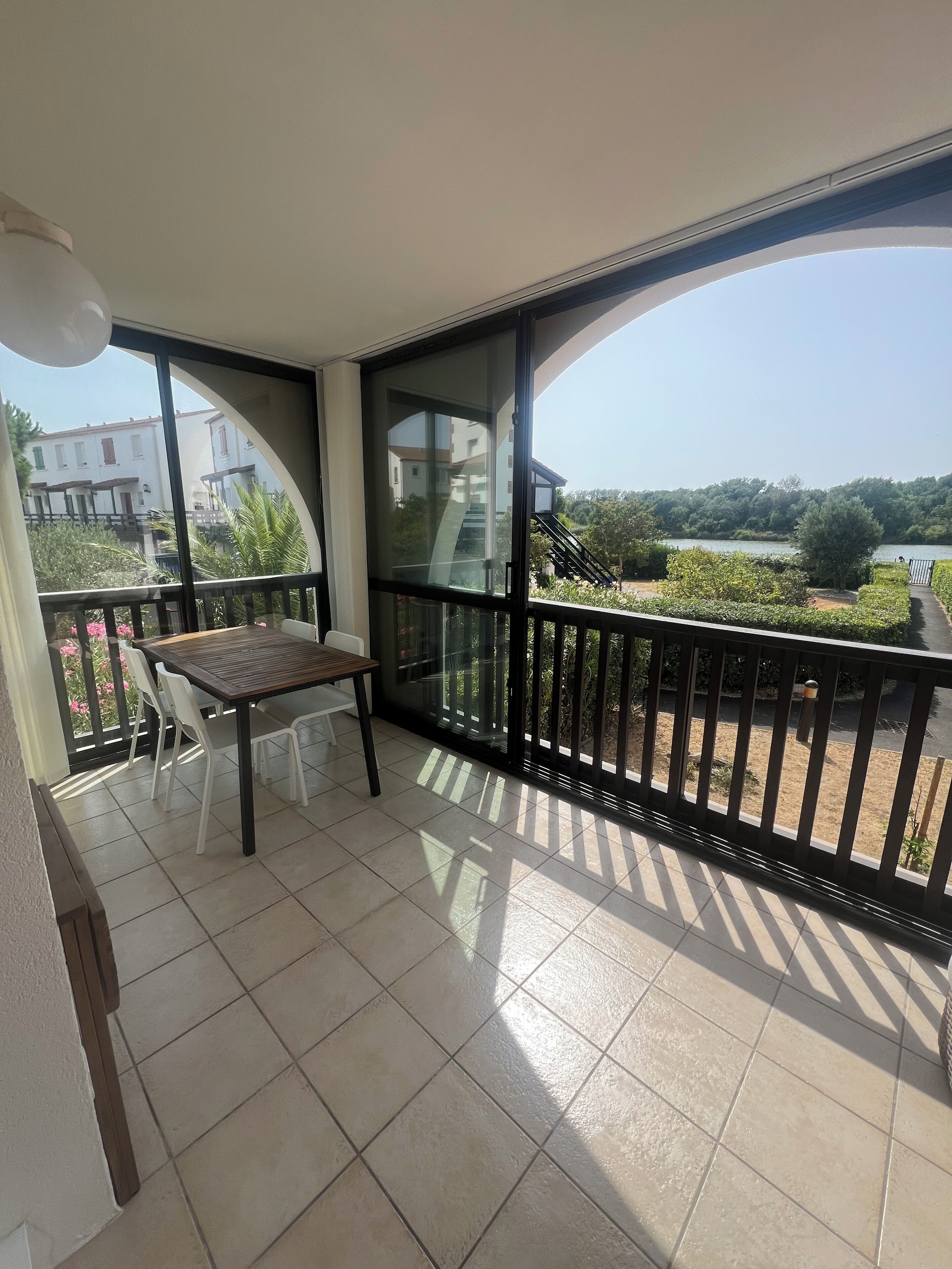 A balcony with a table and chairs, a view of a lake, and a building in the background.