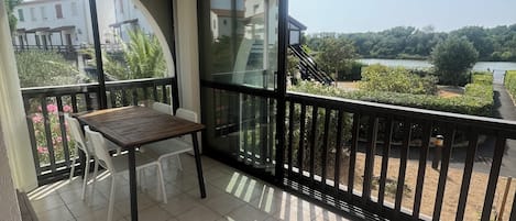 A balcony with a table and chairs, a view of a lake, and a building in the background.