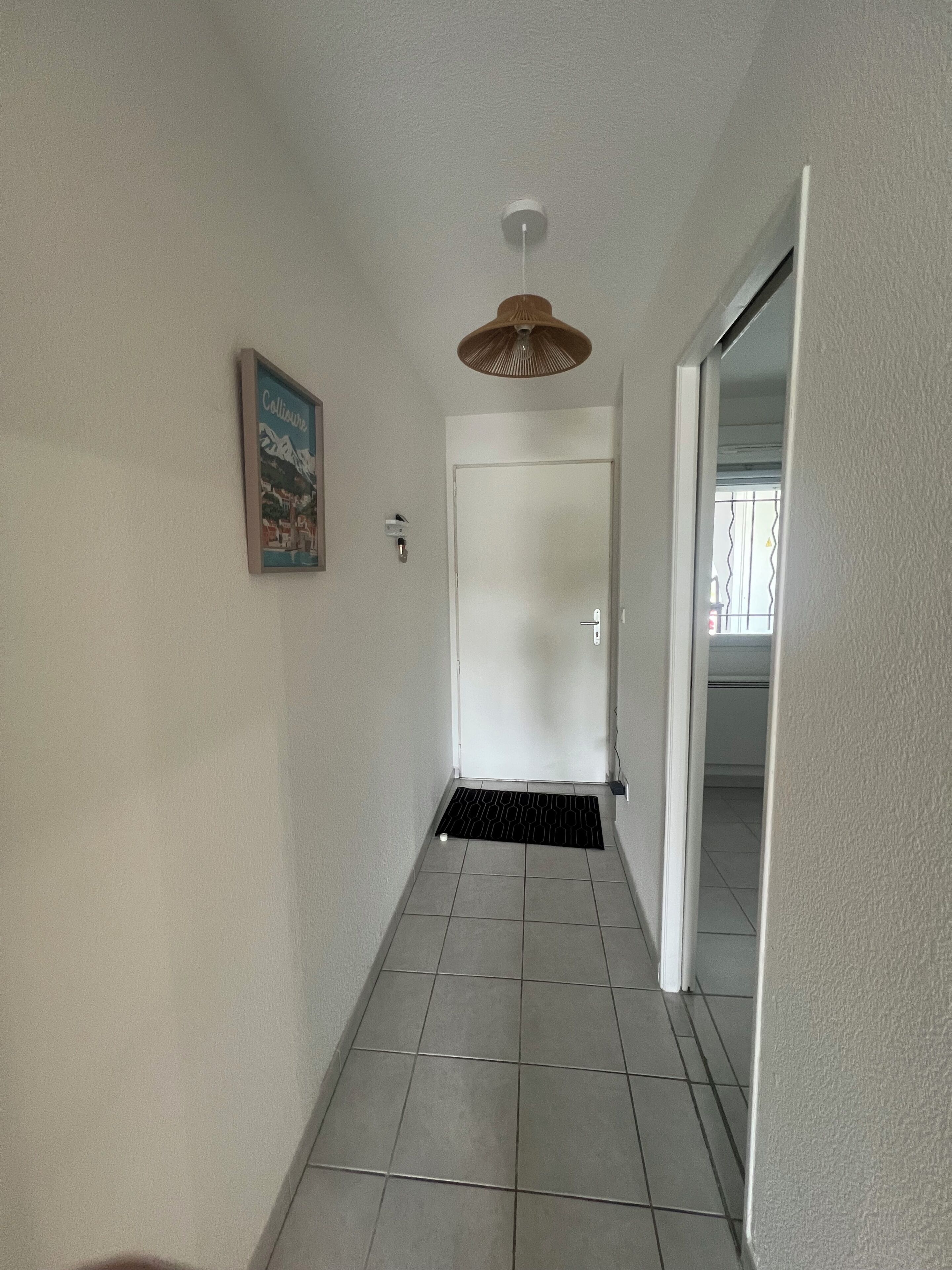 A hallway with a door, a wall-mounted light fixture, and a tiled floor.