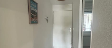 En hall med en dörr, en väggmonterad lampa och ett klinkergolv.