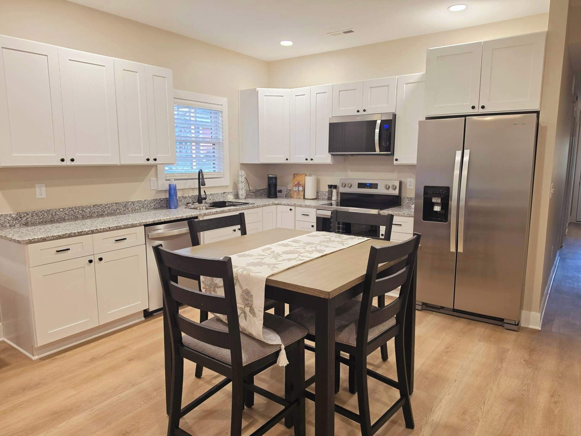 A modern kitchen with white cabinets, a stainless steel refrigerator, a microwave, and a dining table with chairs.