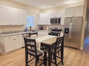 A modern kitchen with white cabinets, a stainless steel refrigerator, a microwave, and a dining table with chairs.