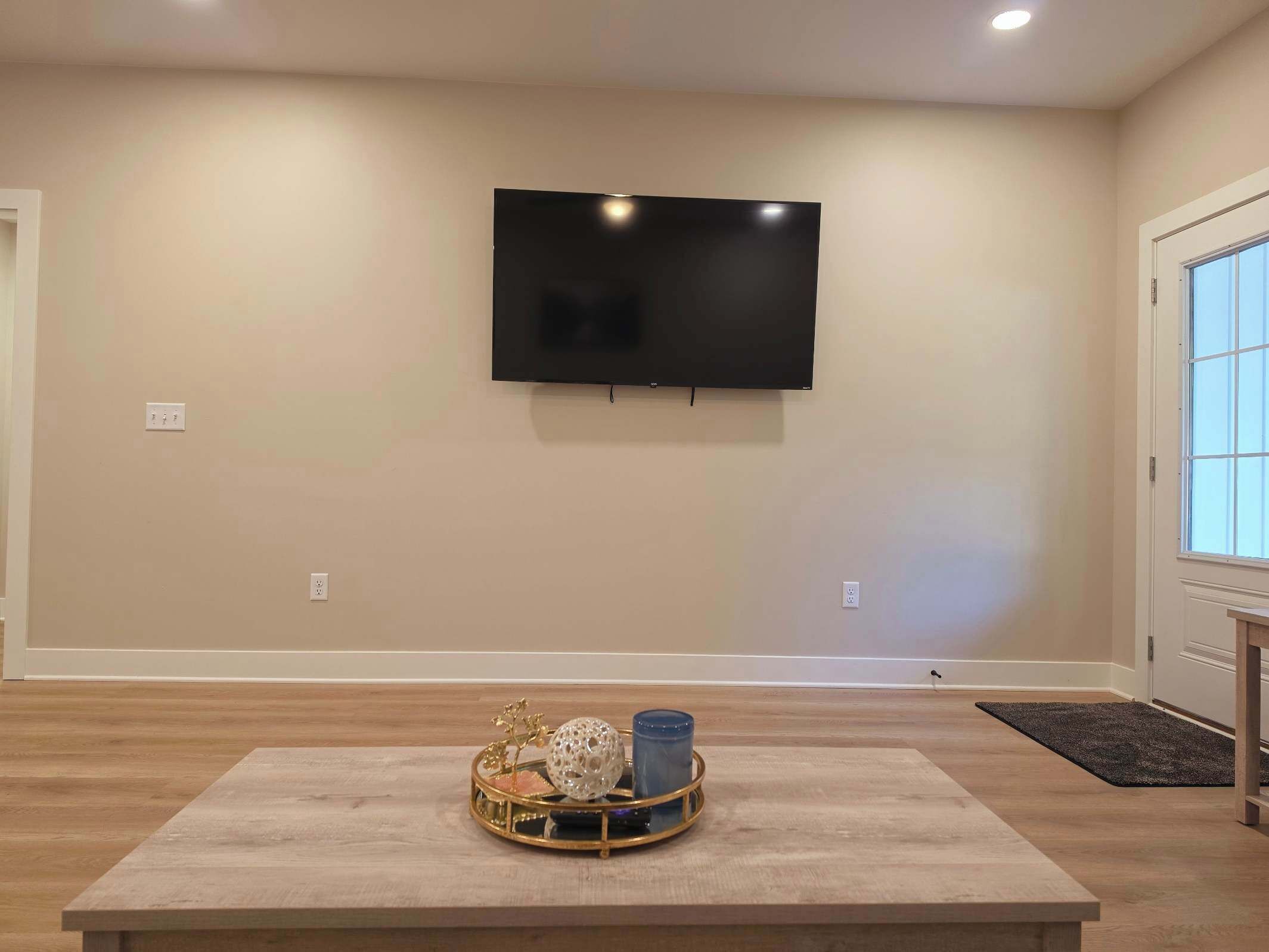 Una sala de estar con un televisor de pantalla plana montado en la pared, una mesa de centro de madera con adornos y un ventanal con vistas.
