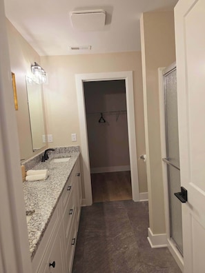 A bathroom with a granite countertop, a mirror, and a shower area.