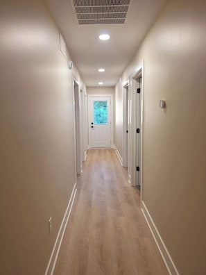A hallway with wooden flooring, white walls, and doors leading to individual rooms.