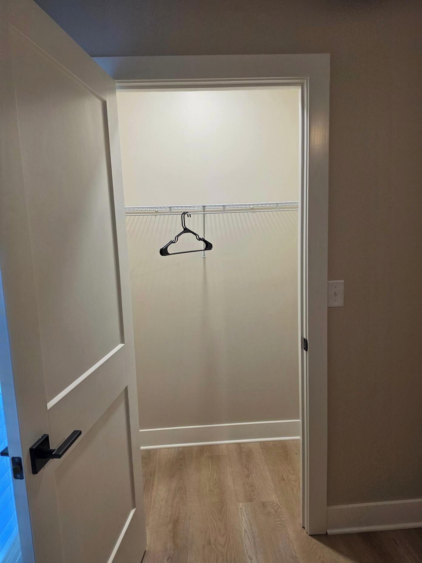 A hallway with a door leading to a room with a wooden floor and a coat rack.