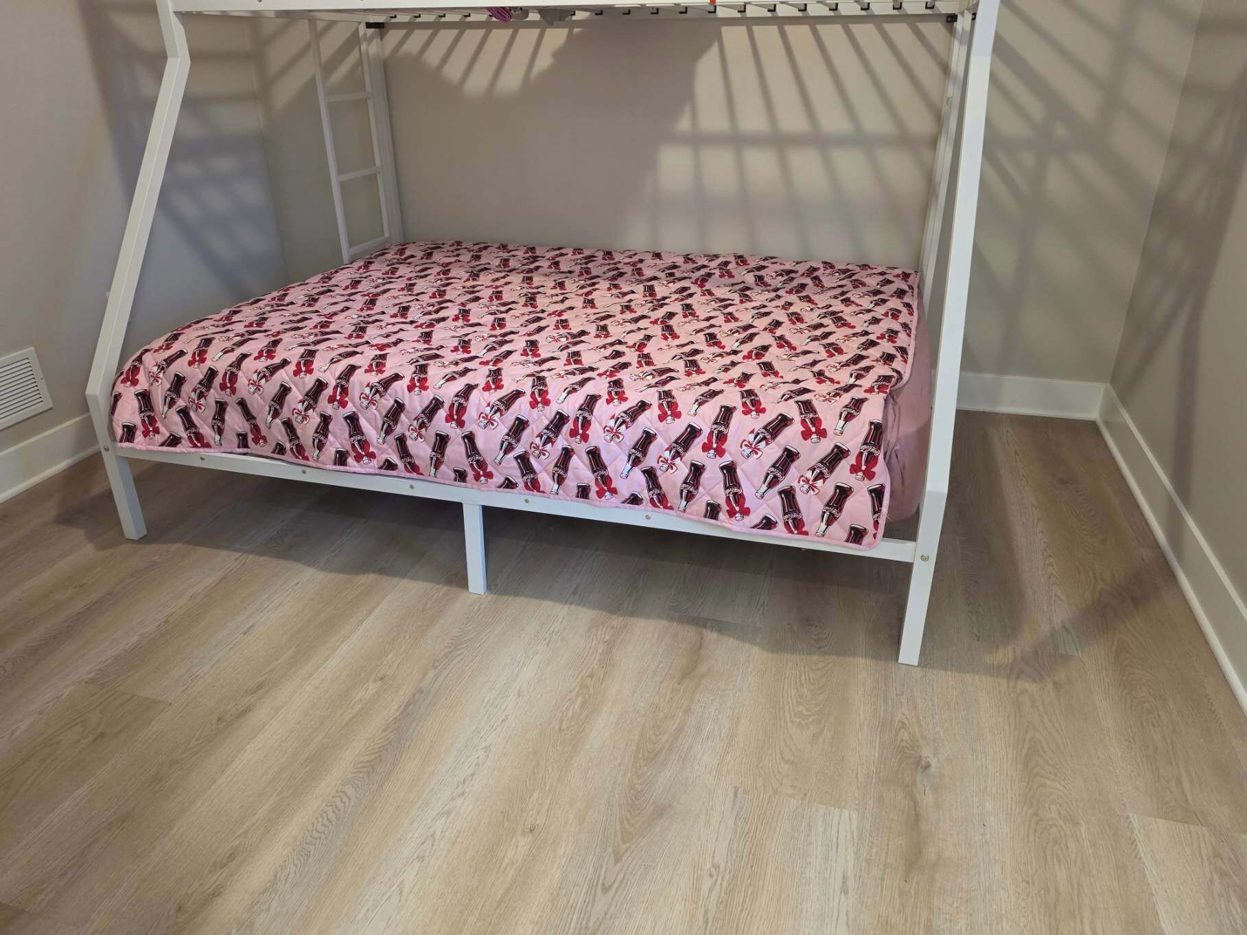 Un lit superposé avec une couvre-lit à motifs dans une pièce dont le sol est recouvert de parquet.