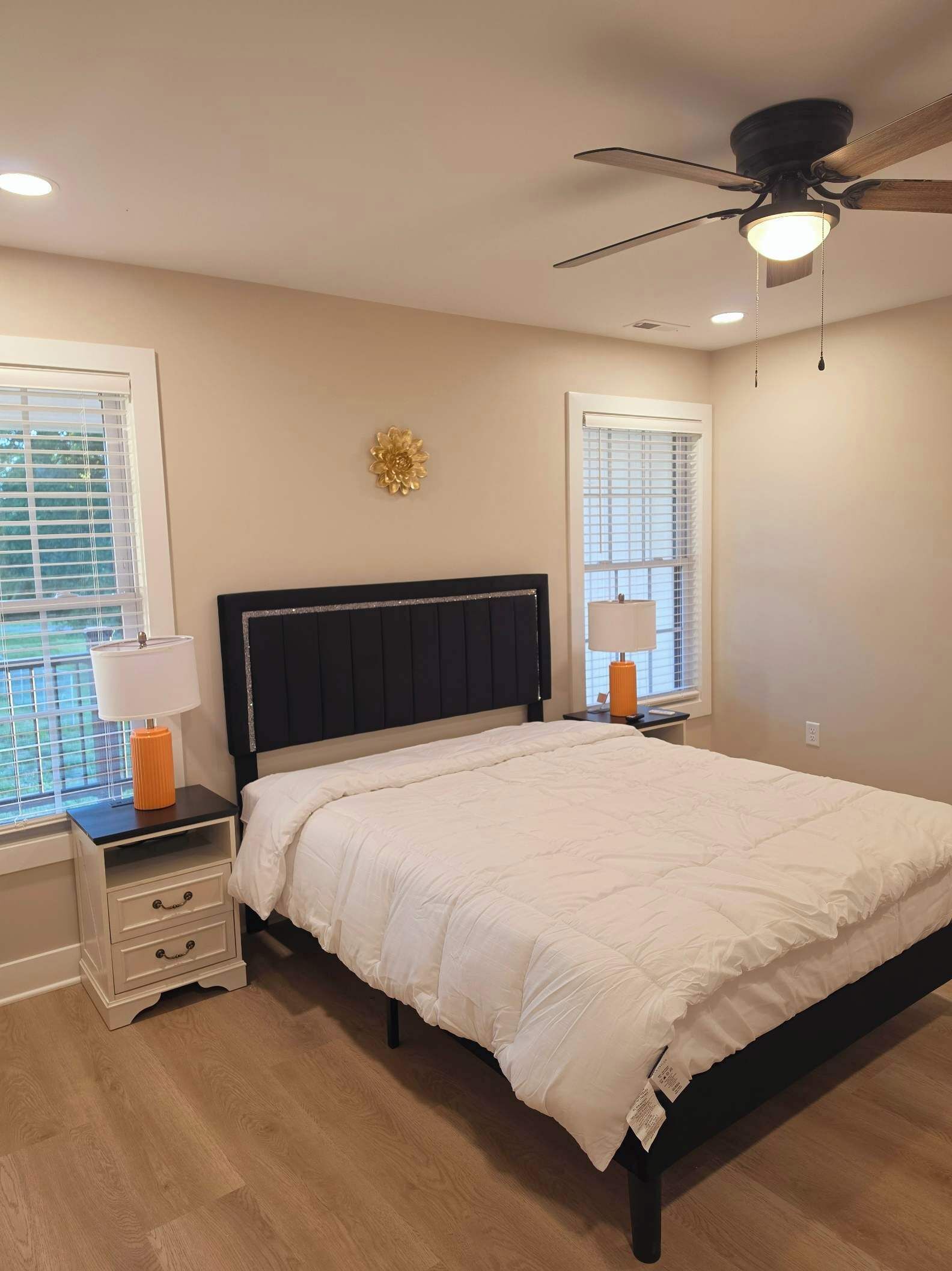 A bedroom with a bed, nightstands, a ceiling fan, and two windows with blinds.