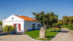 Un edificio bianco con tetto in tegole rosse, vialetto lastricato e area verde con un grande masso.