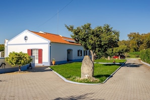 A white building with a red-tiled roof, a paved driveway, and a grassy area with a large rock. - Cottage 'Casa Dos Girassóis' with Shared Pool, Wi-Fi and Air Conditioning (Évora)
