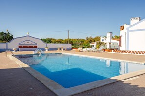 A swimming pool with lounge chairs and a pergola, surrounded by a white building with a tiled roof.
