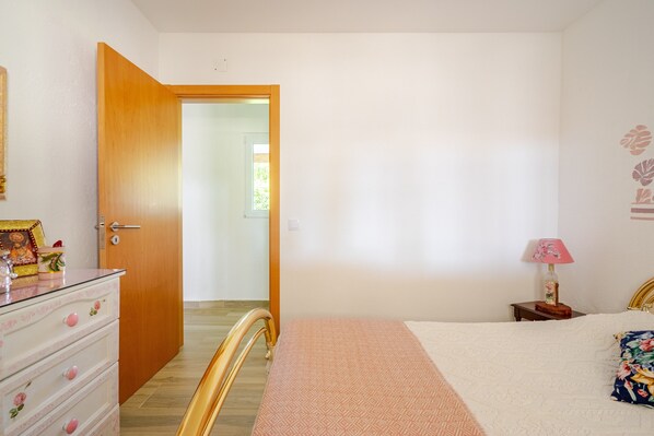 A bedroom with a bed, dresser, and a door leading to another room.