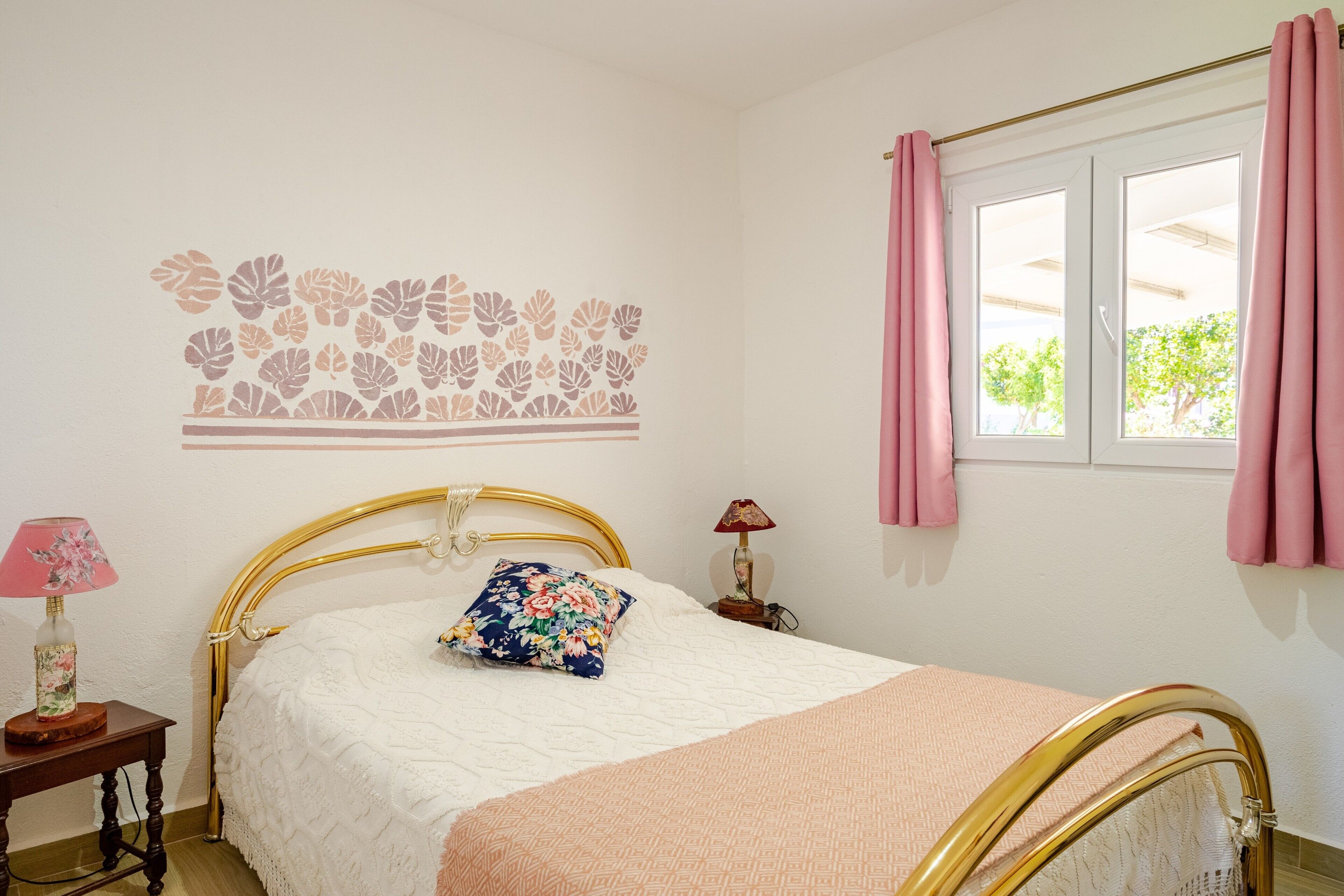 A bedroom with a bed, a nightstand, a lamp, a window with curtains, and a wall decoration.