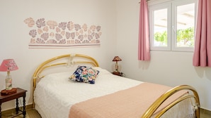 Una camera da letto con un letto, un comodino, una lampada, una finestra con tende e un elemento decorativo al muro.