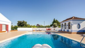 Una piscina con acqua cristallina circondata da un edificio bianco con persiane rosse e una piccola struttura con tetto in tegole.