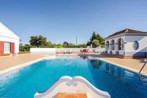 A swimming pool with clear blue water, surrounded by a white building with red shutters, and a small structure with a tiled roof. - Cottage 'Casa Dos Girassóis' with Shared Pool, Wi-Fi and Air Conditioning (Évora)