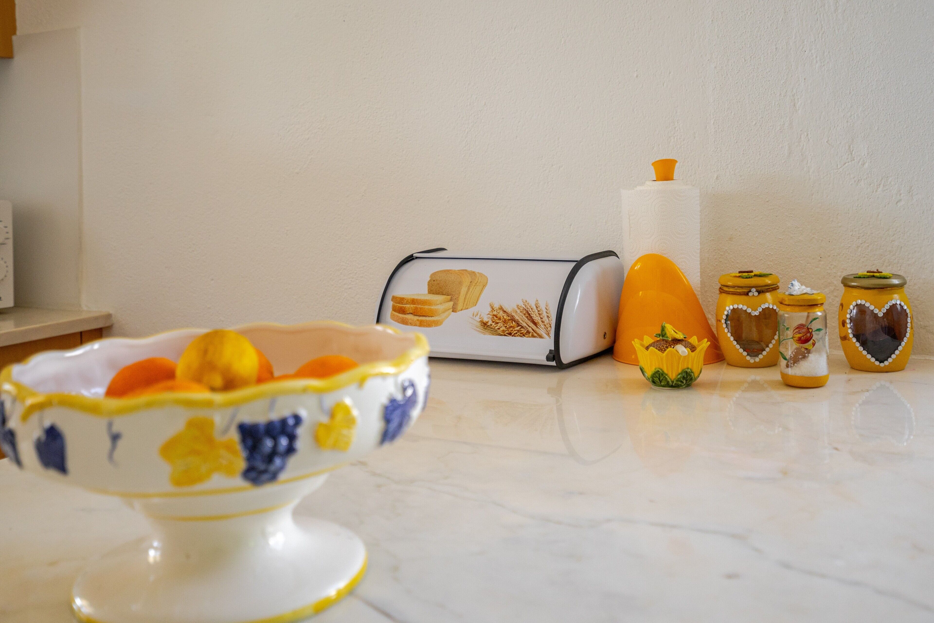 Una encimera de cocina con un bol de fruta, un tostador y dos frascos con tapas decorativas.