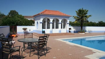 A pool area with a small gazebo, outdoor seating, and a clear blue sky.