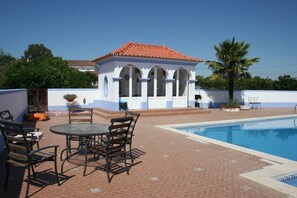 A pool area with a small gazebo, outdoor seating, and a clear blue sky.
