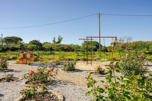 A garden with a wooden playhouse, a swing set, and a variety of flowering plants.