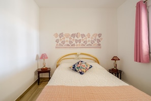 A bedroom with a bed, two bedside tables, a decorative wall, and a pink curtain.