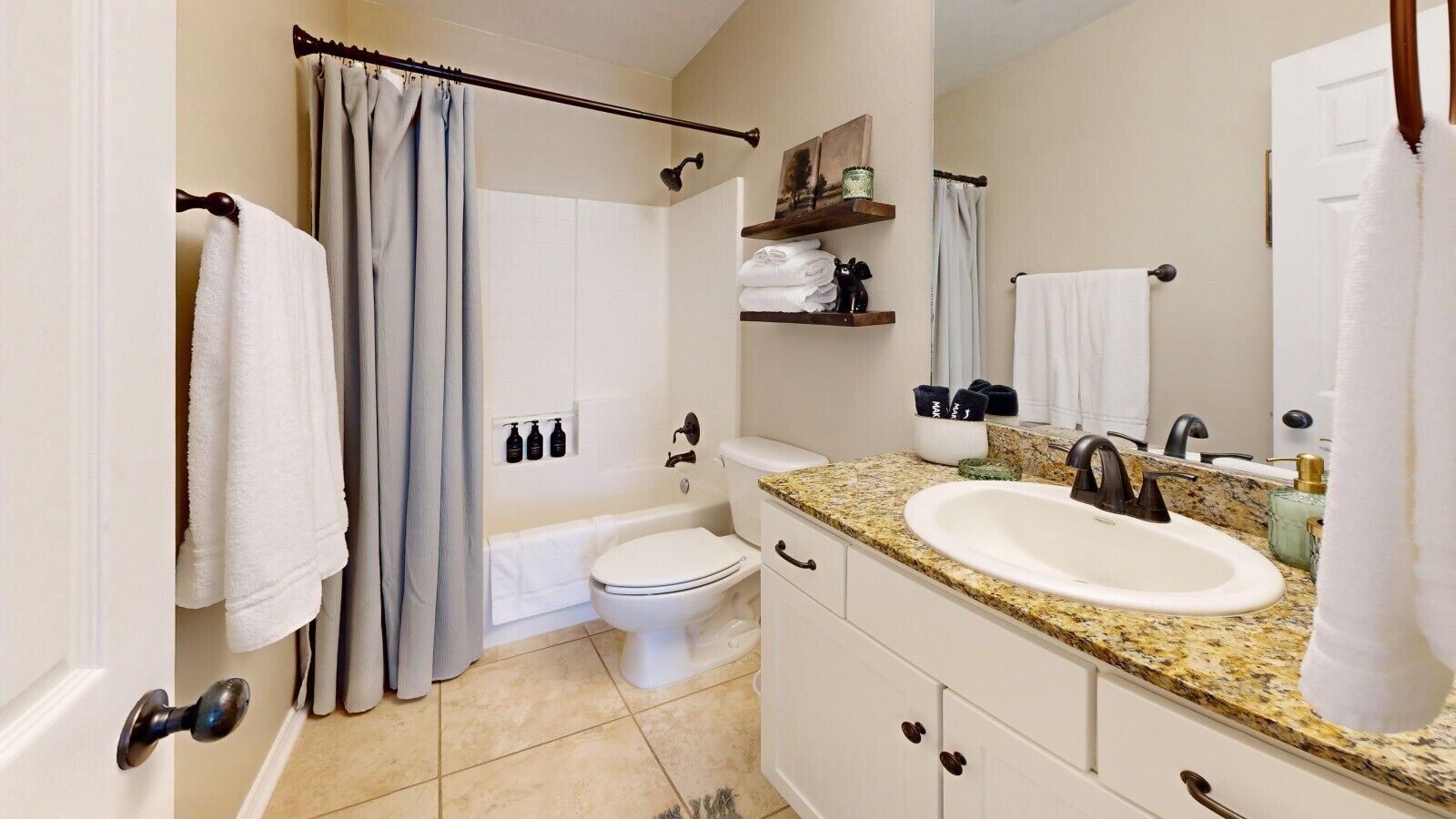 A bathroom with a white toilet, a sink with a granite countertop, and a shower curtain.