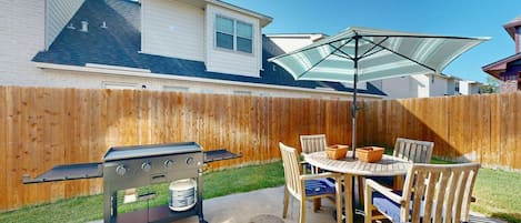 An outdoor patio with a grill, dining table, chairs, and a large umbrella.