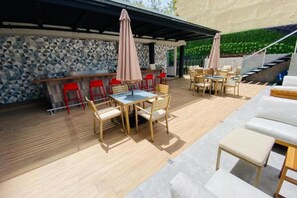 An outdoor patio with wooden tables and chairs, a bar area, and a staircase leading to an upper level. - EON Zone 10 | Luxury, Views, and Comfort—All in One Apartment (Ciudad de Guatemala)