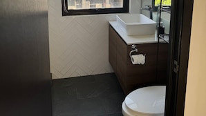 Un baño con un lavabo blanco, baldosas oscuras y un inodoro.