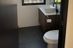 Een badkamer met een wit wastafelmeubel, donkere tegels en een toilet.