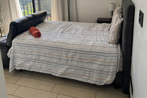 Een slaapkamer met een bed, een zwarte leren fauteuil, een nachtkastje met een lamp en een raam met gordijnen.