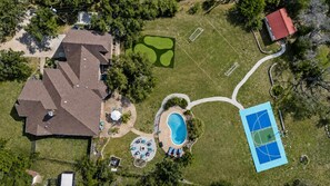 Vista aérea de una propiedad residencial con piscina, cancha de tenis y una casa grande.