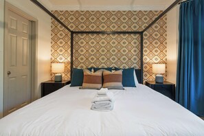 Ein Hotelzimmer mit einem großen Bett, zwei Nachttischen mit Lampen, strukturierter Wandtapete und einer Tür.