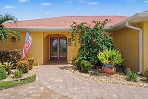 A building with a red roof, a yellow facade, and a front entrance with double doors. - Back Porch Social | Pool, Waterfront, Tiki Bar (Cape Coral)