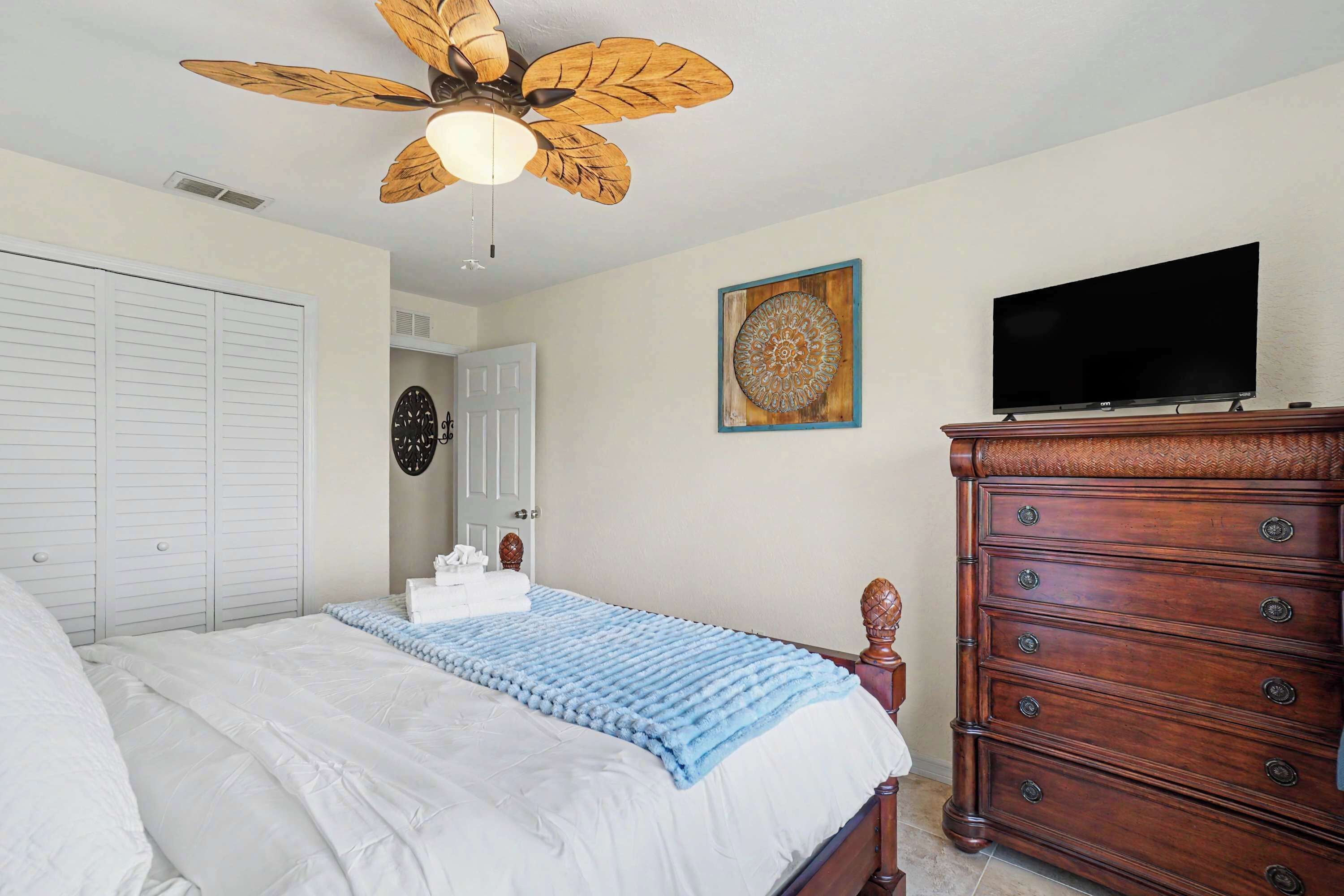 A bedroom with a bed, a dresser, a television, a ceiling fan, and a door.