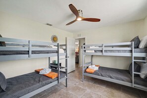 A room with bunk beds, a ceiling fan, and a door leading to another room. - Back Porch Social | Pool, Waterfront, Tiki Bar (Cape Coral)