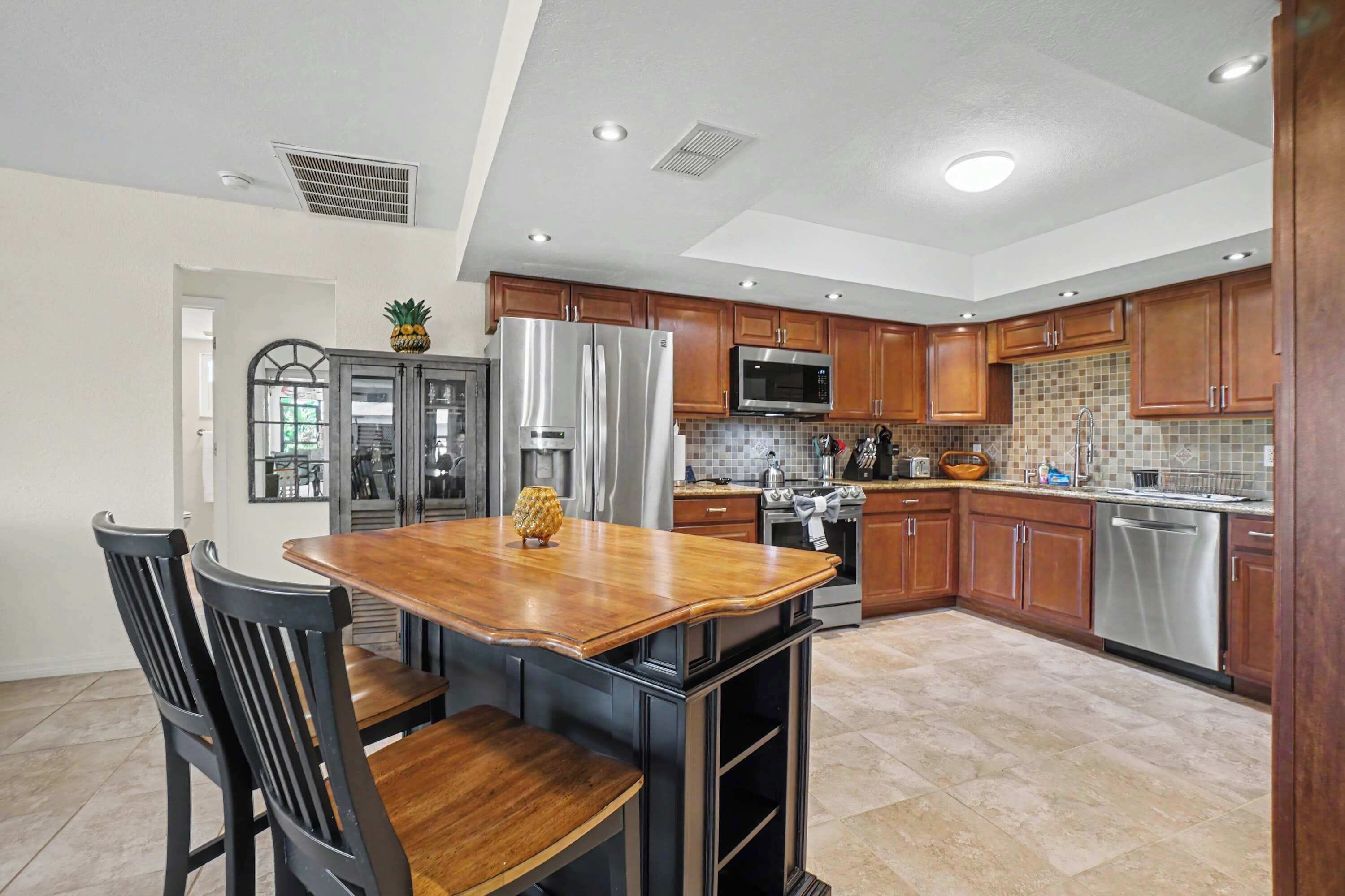 A modern kitchen with a central island, wooden cabinets, stainless steel appliances, and a tiled backsplash.