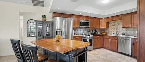 A modern kitchen with a central island, wooden cabinets, stainless steel appliances, and a tiled backsplash.