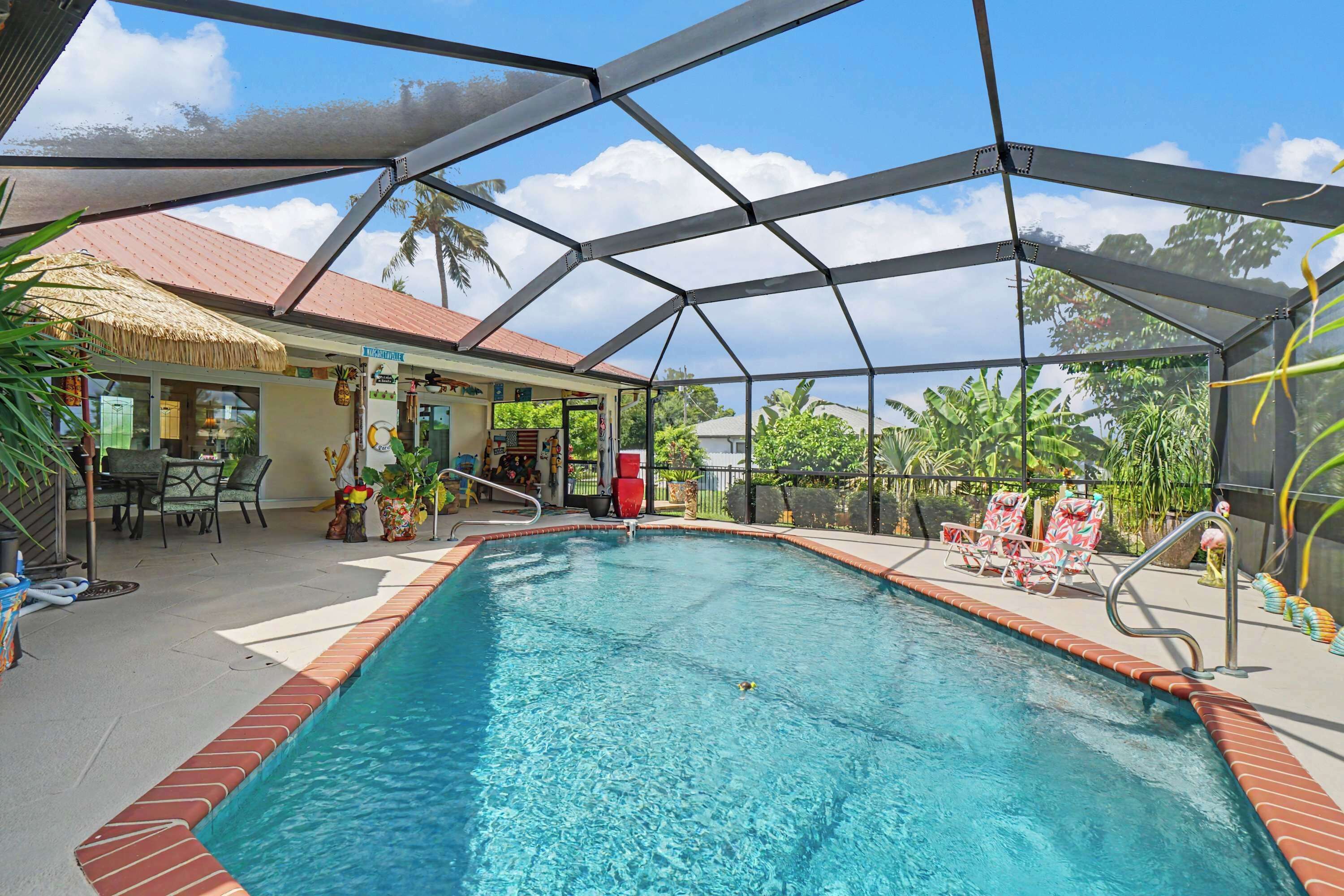 A covered swimming pool with a thatched roof structure, surrounded by lounge chairs and a patio area.