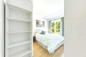 Quarto com cama, mesa de cabeceira, janela com cortinas e prateleira na parede.
